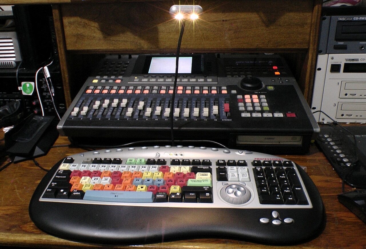 A colour-coded editing keyboard in front of an audio mixing console.