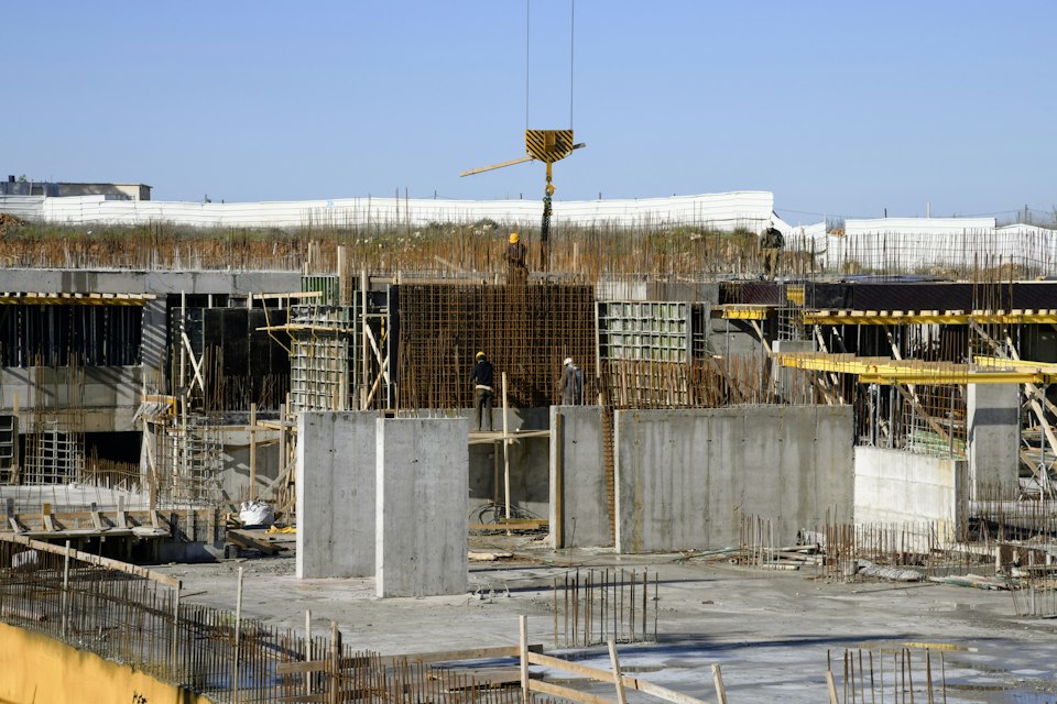 Concrete columns and reinforcing steel on a building site beneath a crane hook.